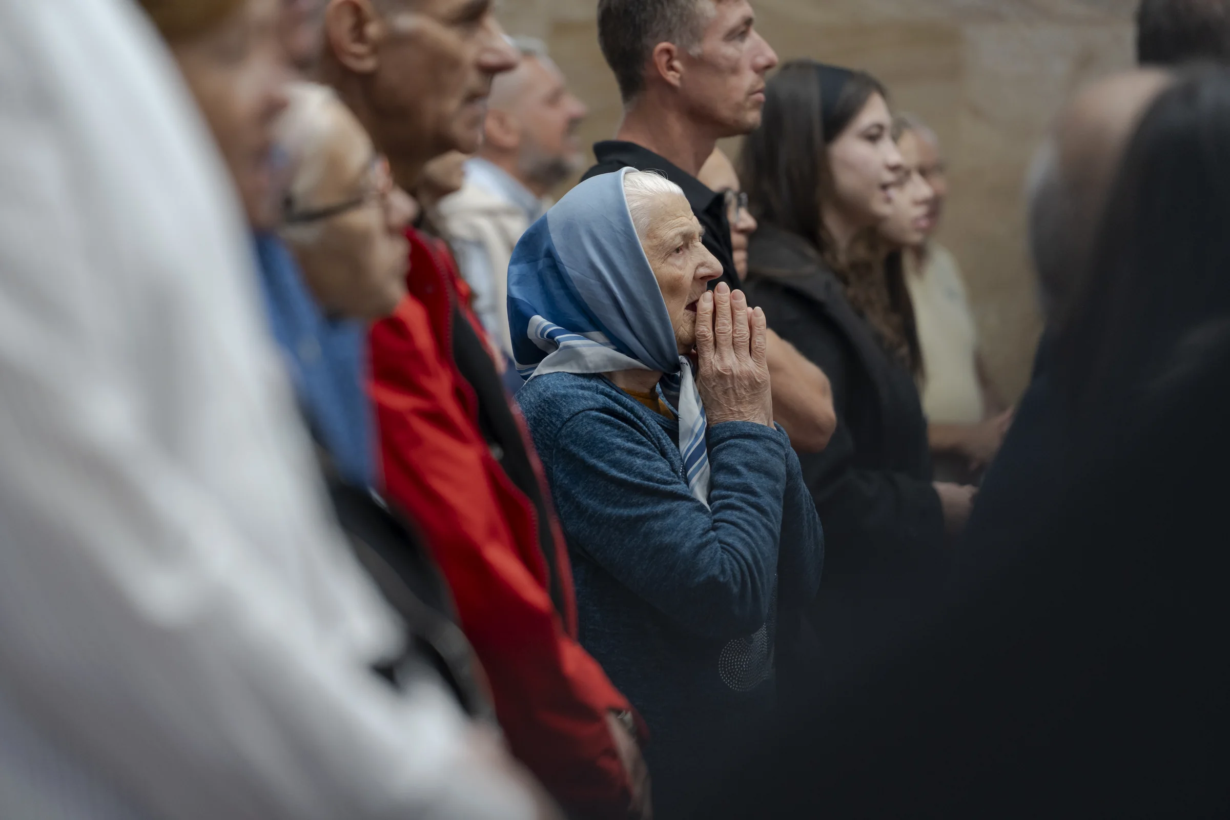 O bătrână se roagă cu mâinile împreunate, în mijlocul bisericii